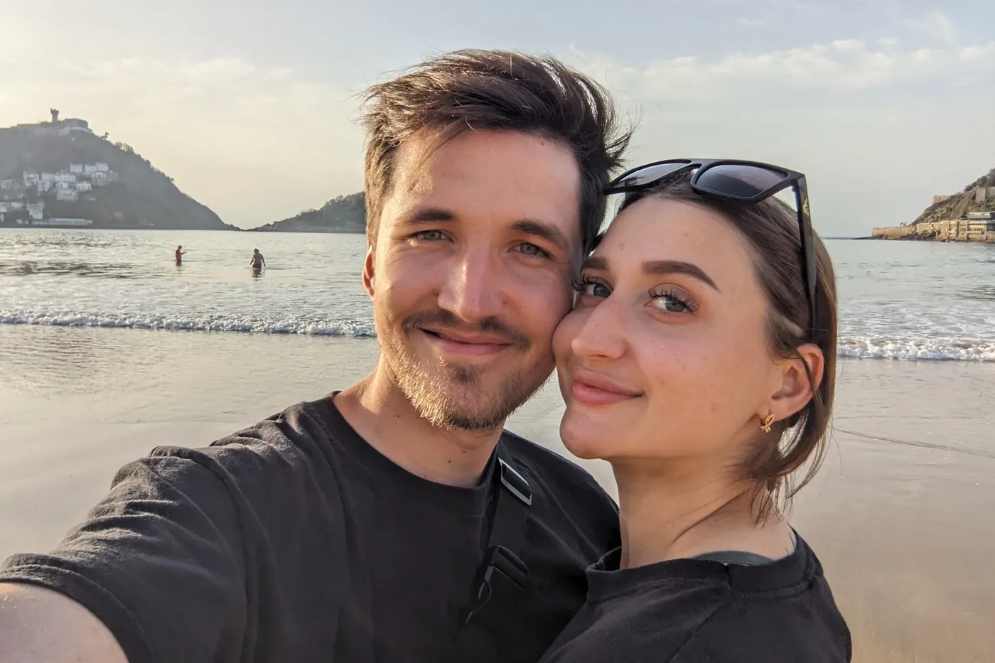 Alona und Jan Wange an Wange am Strand von San Sebastián, hinter ihnen die Bucht und das Meer